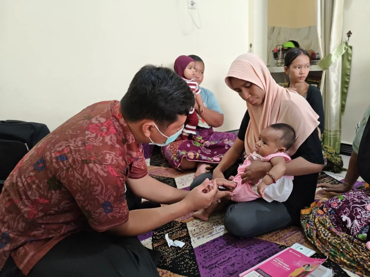Petugas mengimunisasi bayi yang dipangku ibunya
