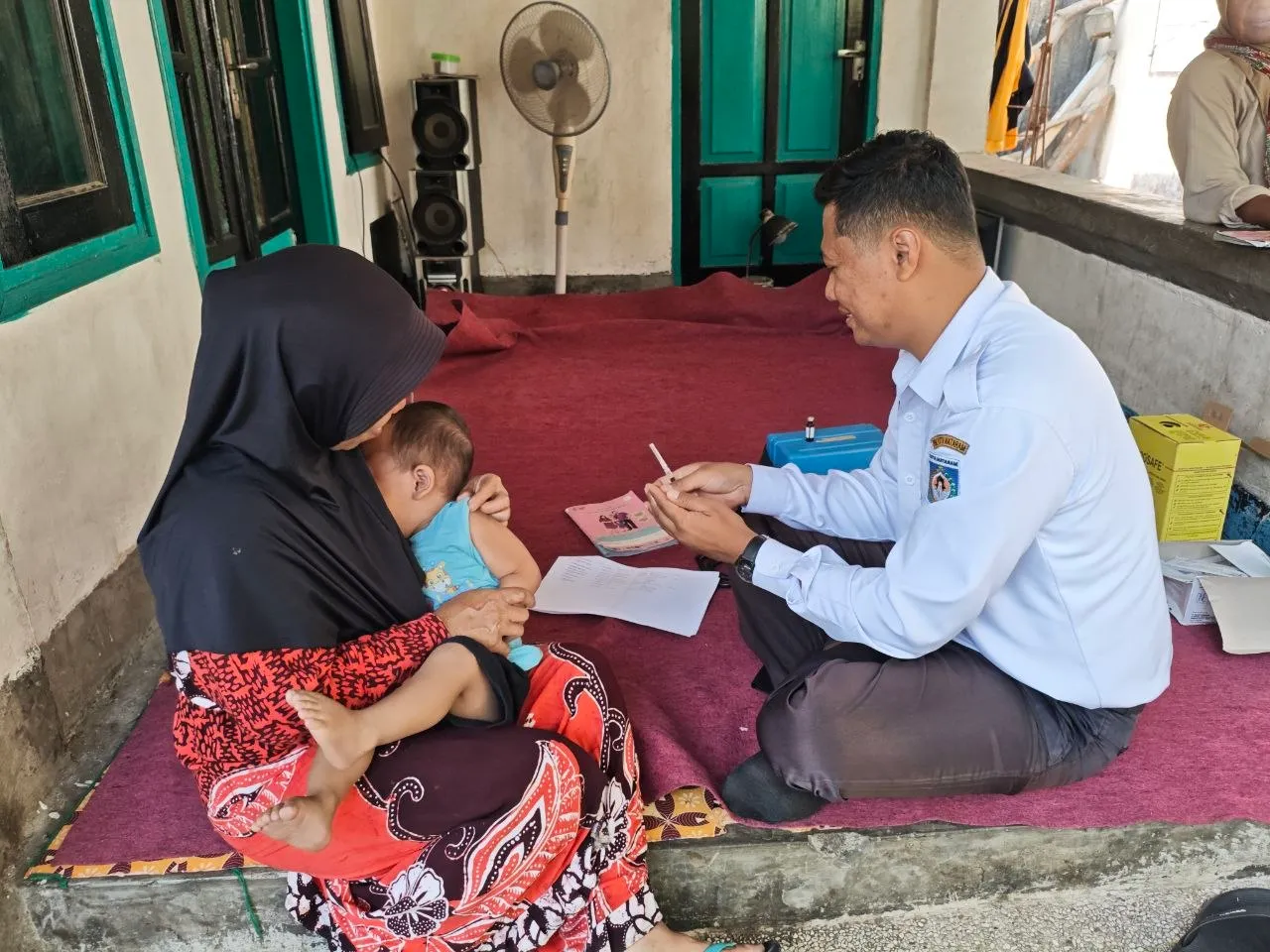Petugas mencatat di teras rumah, ditemani ibu yang memangku bayinya