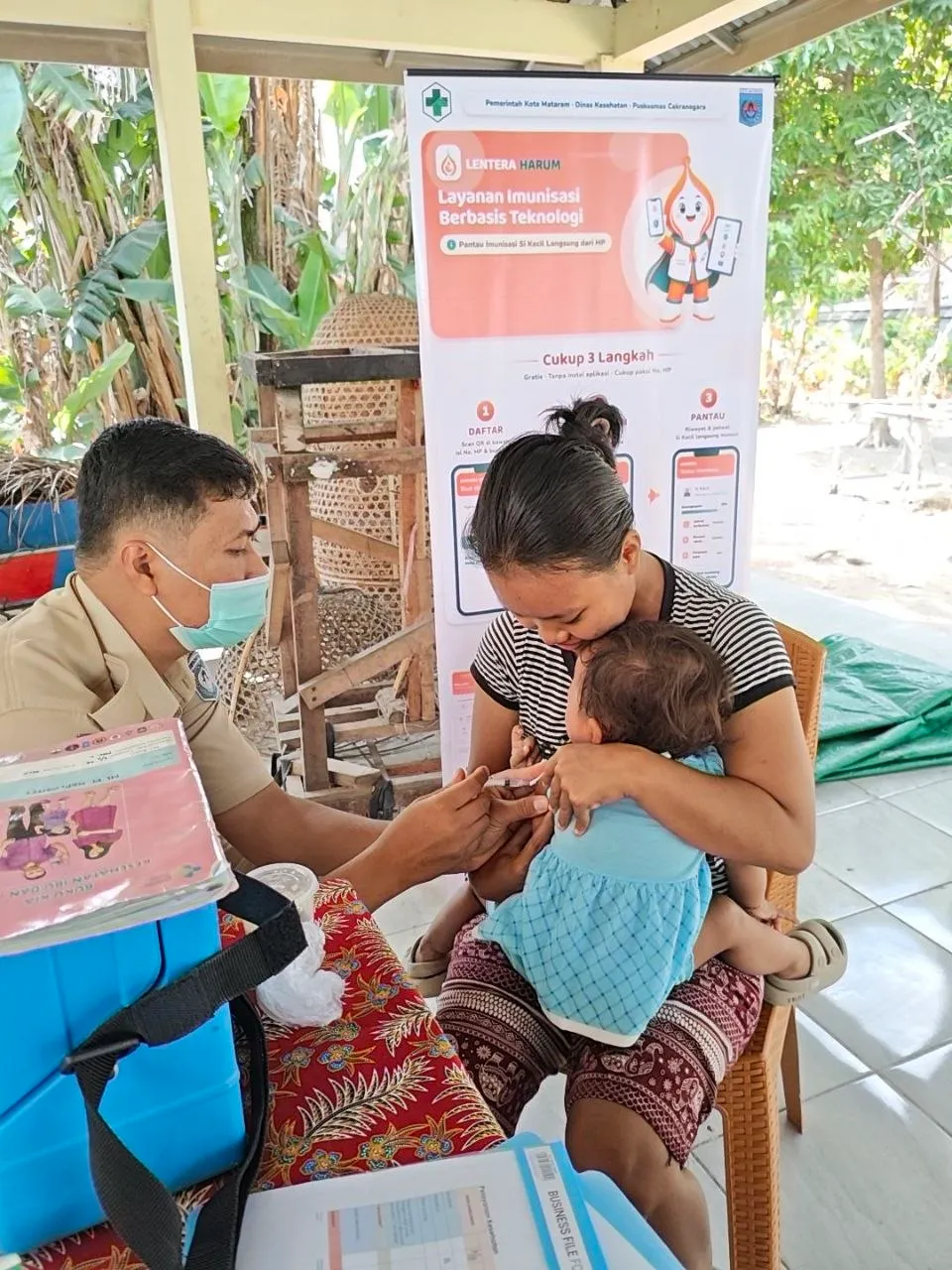 Petugas mengimunisasi bayi di posyandu, dengan banner LENTERA HARUM di belakangnya